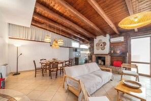 A spacious living area with a wooden ceiling, a dining table set for four, a sofa, and a fireplace. - Casa di Adriana&Claudia, Porto Cesareo, Italy (Porto Cesareo)
