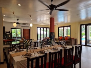 Uma sala de jantar com uma mesa comprida posta para uma refeição, rodeada de cadeiras.