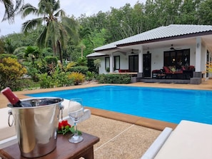Área da piscina com vista para uma casa, uma mesa com bebida e cadeiras de descanso.