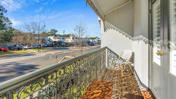 Un balcone con ringhiera in metallo, una sedia e vista su una strada con auto e palazzi.