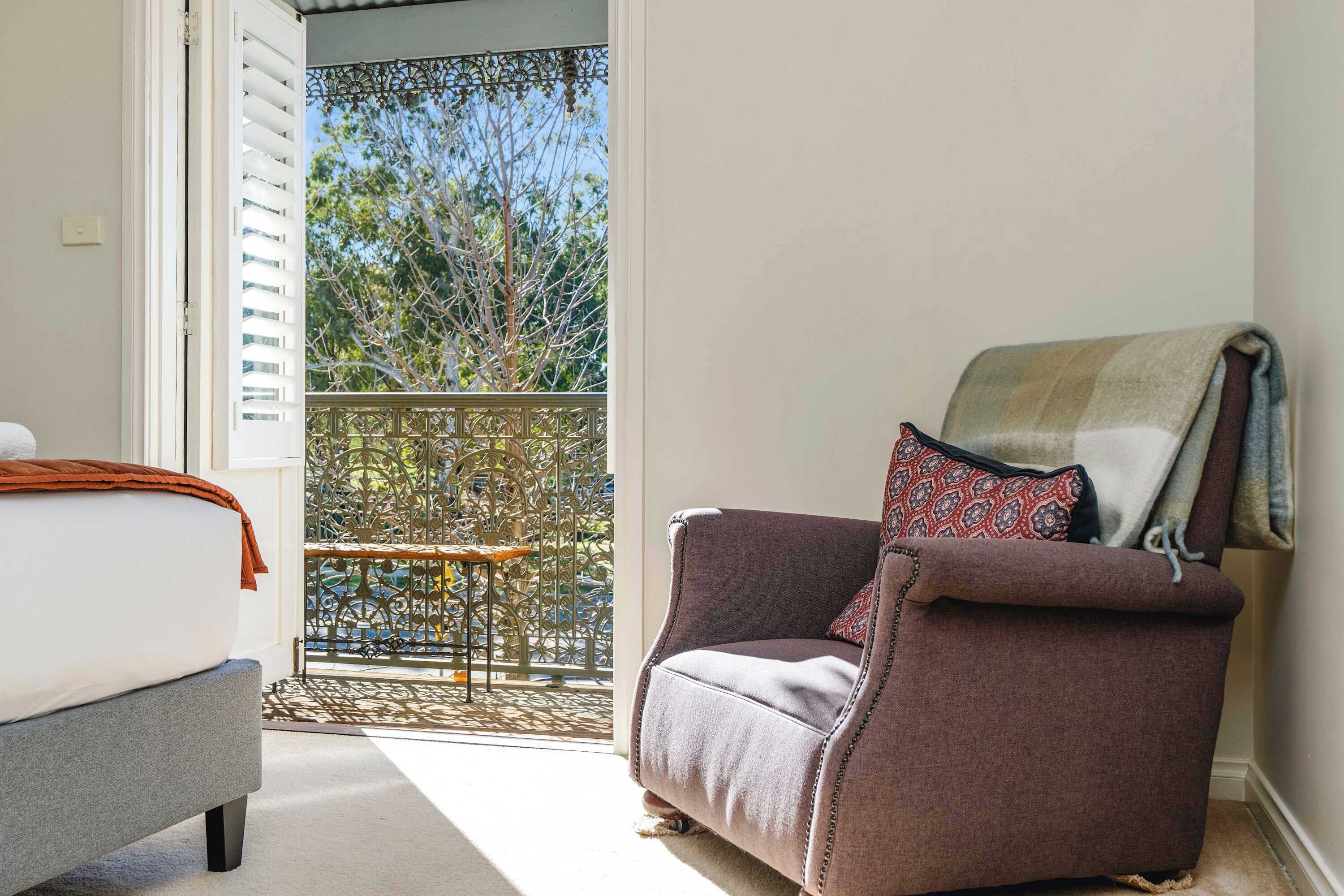 A room with a bed, a chair, and a view of a balcony with a tree.