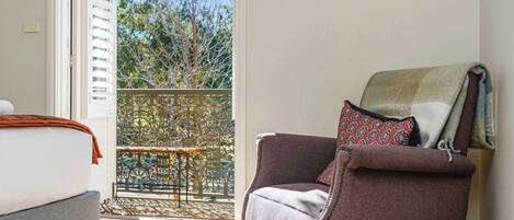 A room with a bed, a chair, and a view of a balcony with a tree.
