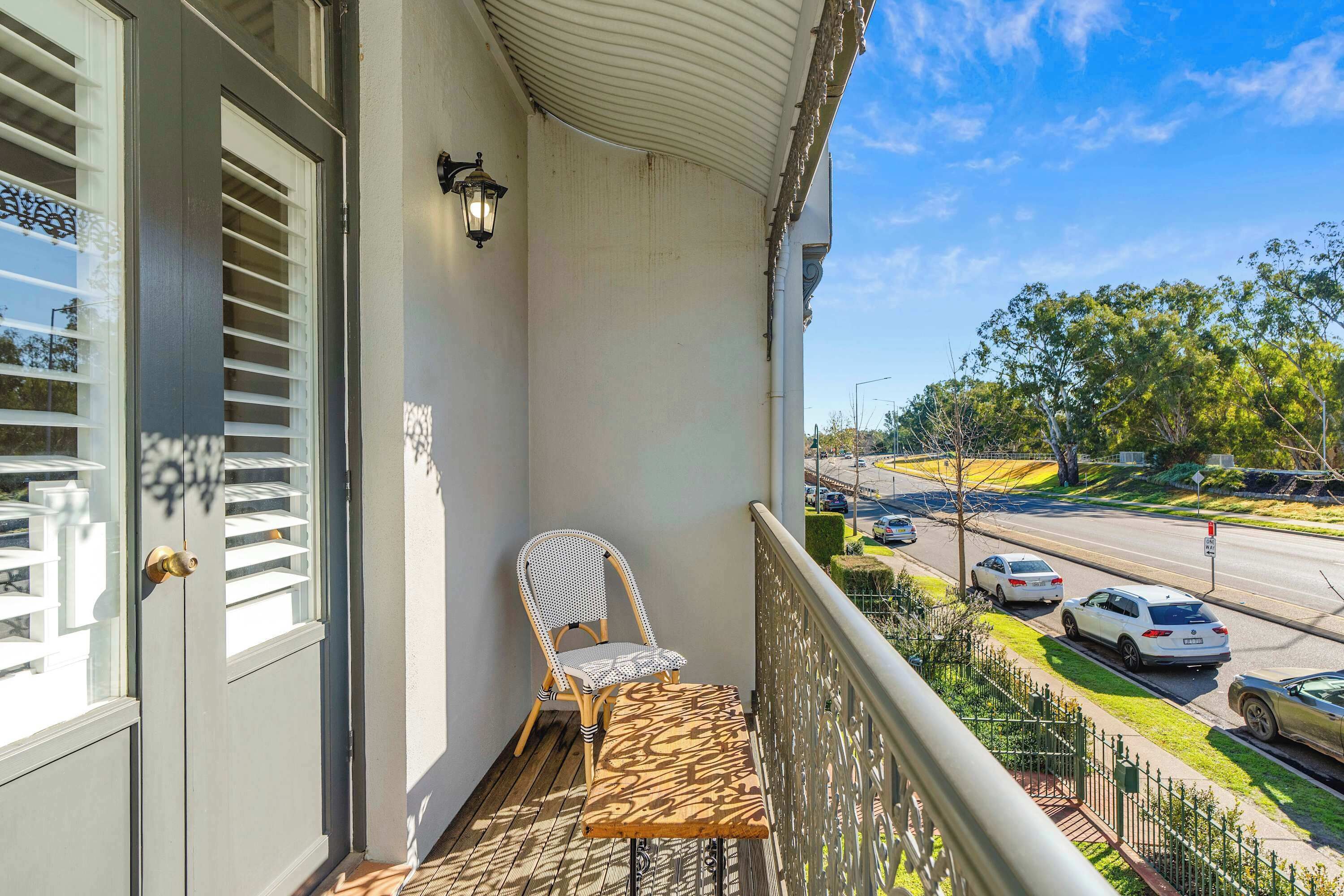 A balcony with a chair and table, overlooking a street with cars and trees.