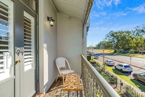 A balcony with a chair and table, overlooking a street with cars and trees.