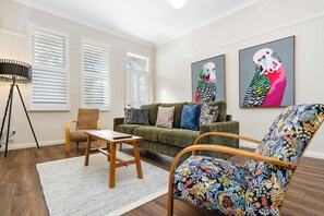 A living room with a green sofa, a wooden coffee table, a patterned armchair, and two wall-mounted paintings.
