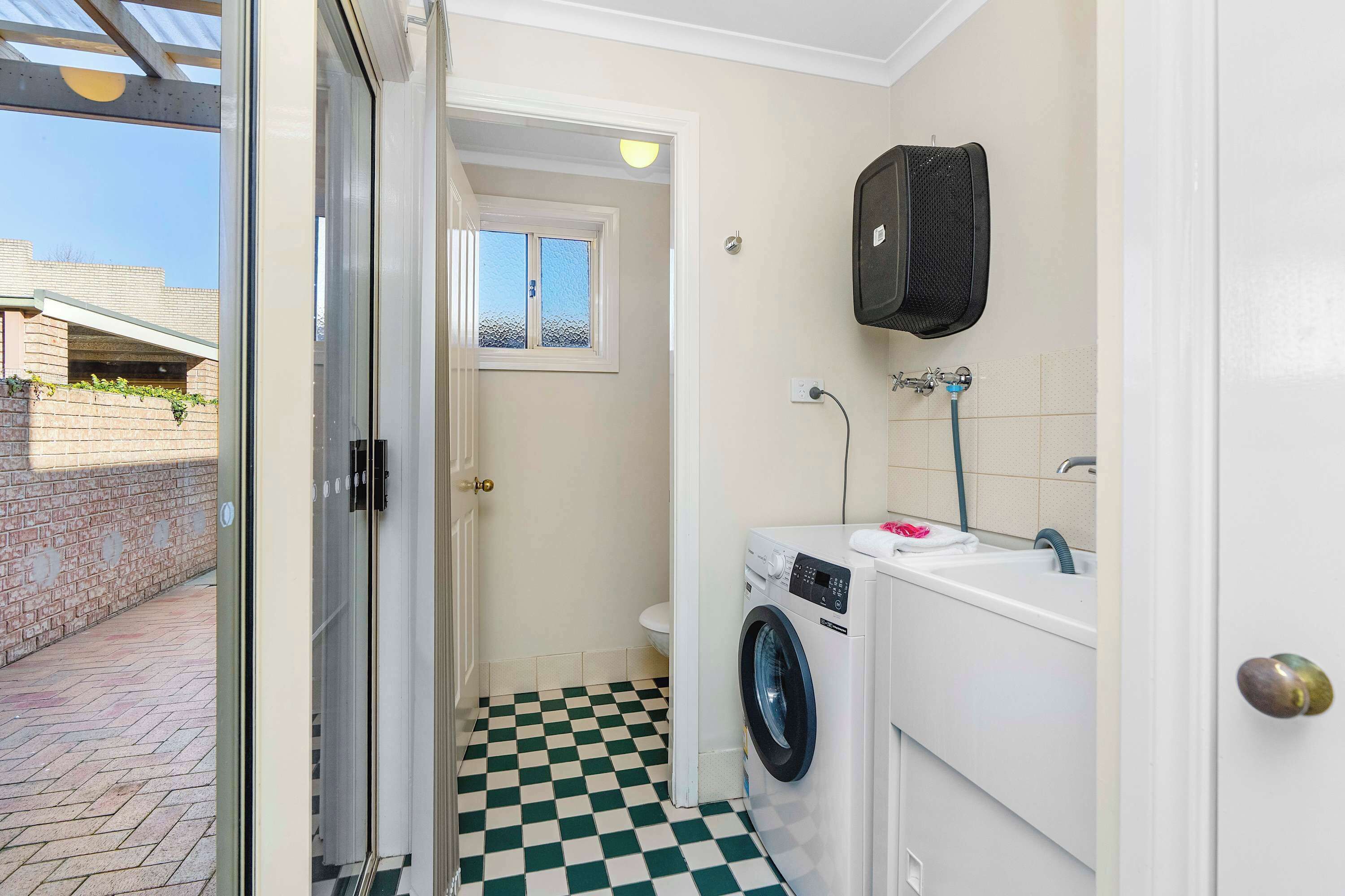 A compact laundry room with a washing machine, a sink, and a window.