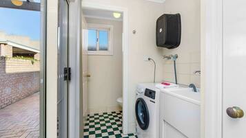 A compact laundry room with a washing machine, a sink, and a window.