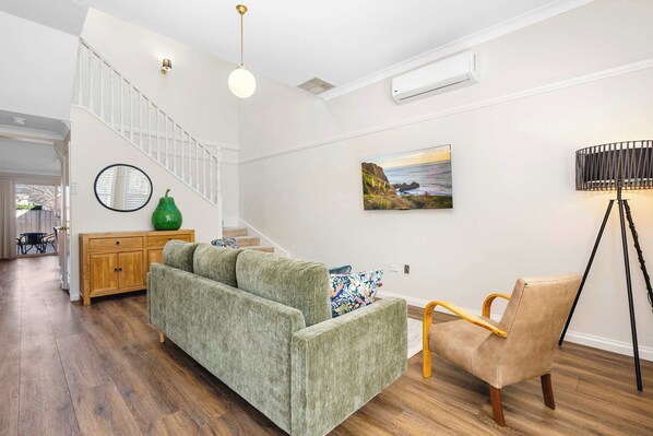 A living room with a sofa, a chair, a floor lamp, a painting, and a staircase.