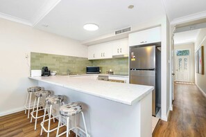 A modern kitchen with a central island, bar stools, a stainless steel refrigerator, and a microwave.