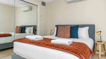 A hotel room with a bed, a bedside table with a lamp, a mirror, and an air conditioning unit on the wall.