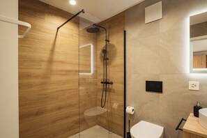 Ein modernes Badezimmer mit Holzvertäfelung, einer Glasdusche, einer Toilette und einem Waschbecken.
