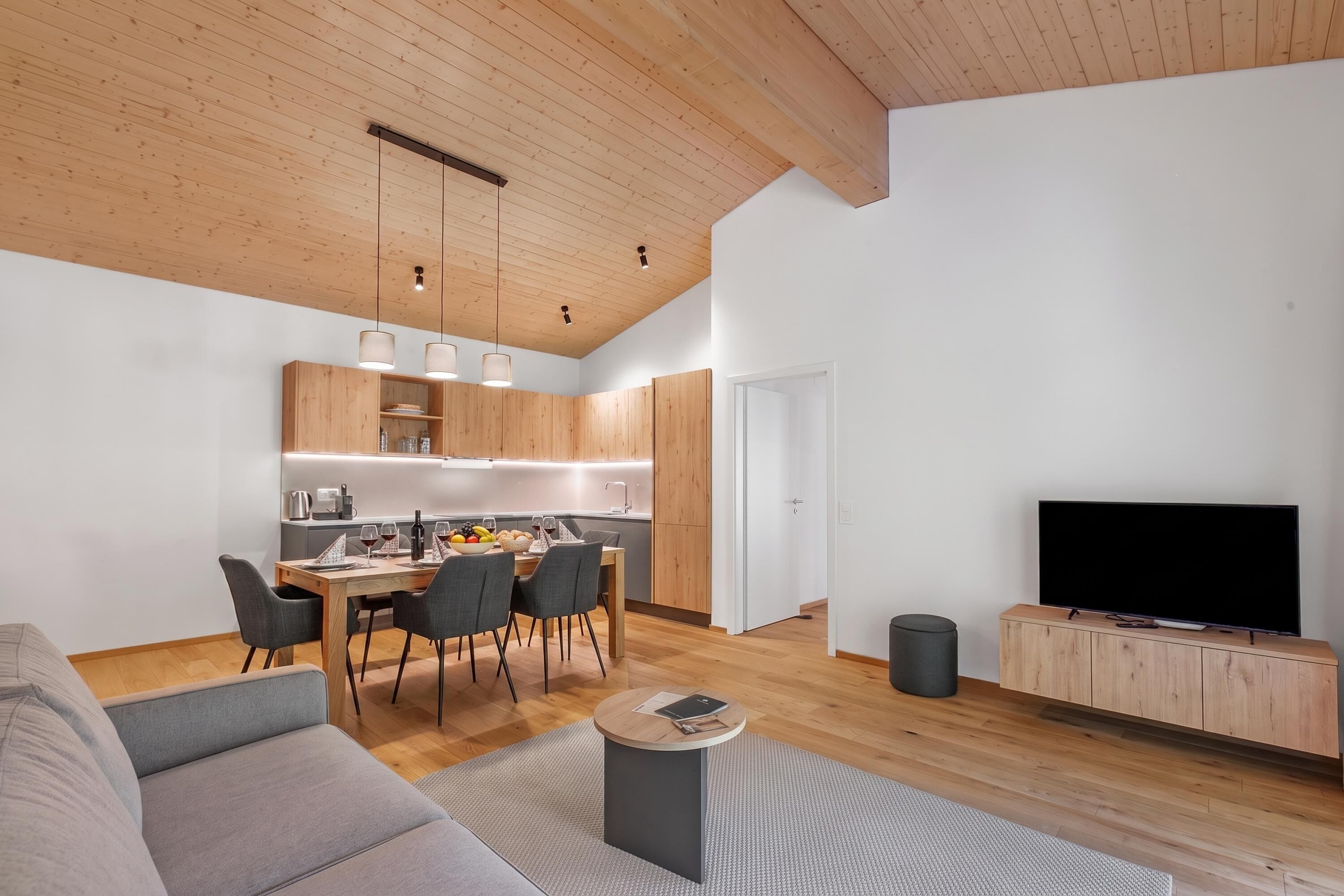 Una sala moderna con un sofá, una mesa de comedor con sillas, una zona de cocina y un televisor.