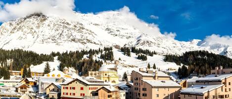 Une ville de montagne recouverte de neige, avec des bâtiments et des voitures garées.