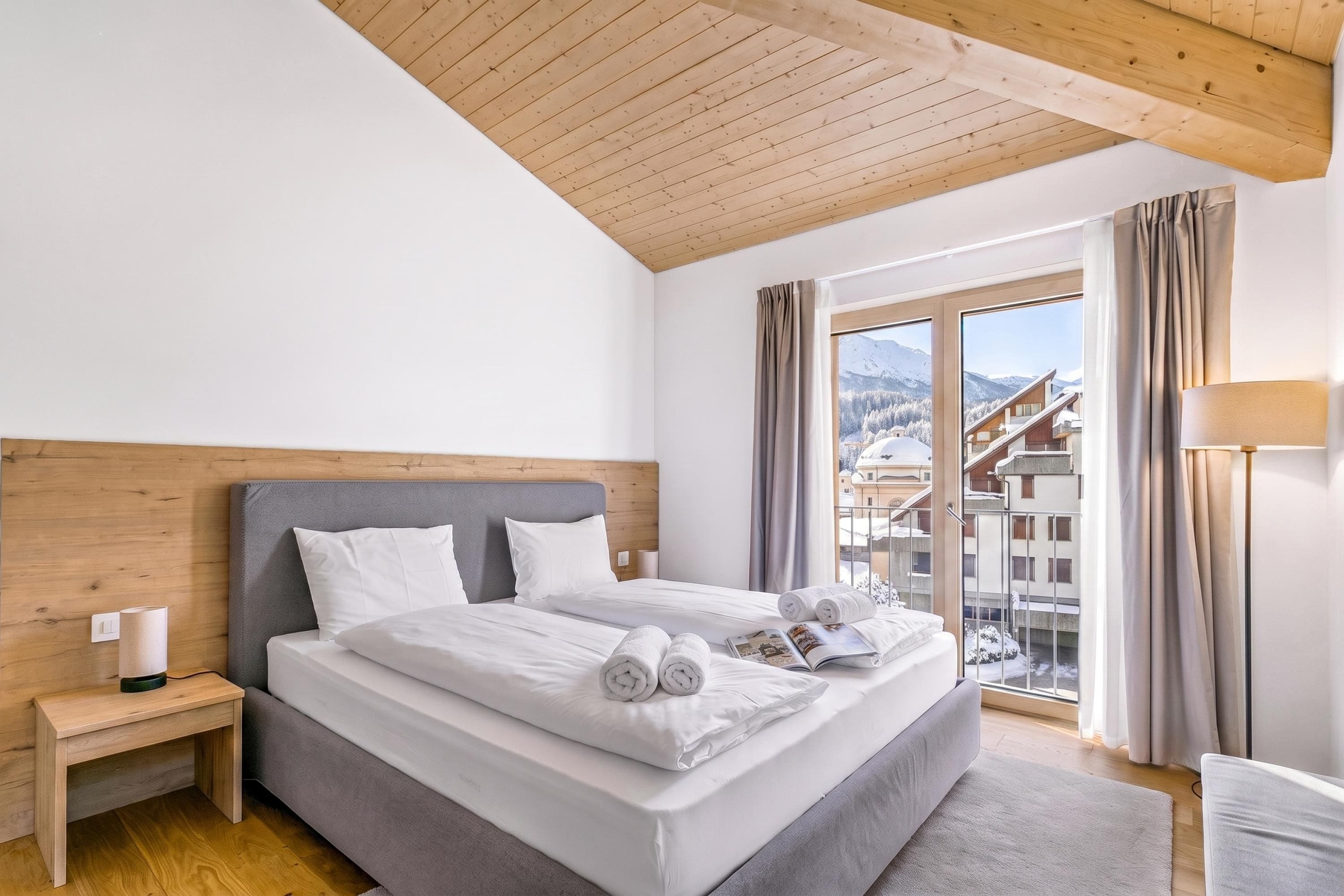 A hotel room with a bed, a nightstand, a lamp, and a view of a snowy mountain landscape.