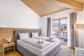 A hotel room with a bed, a nightstand, a lamp, and a view of a snowy mountain landscape. - Residenza Castanea 308 San Bernardino Alpine Apartments, San Bernardino, Switzerland (San Bernardino)