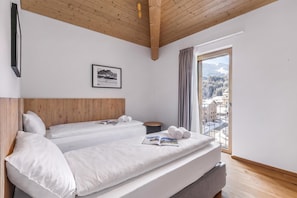 Ein Hotelzimmer mit zwei Betten, einer Holzbalkendecke, einem gerahmten Bild an der Wand und Blick auf eine verschneite Landschaft durch ein Fenster.