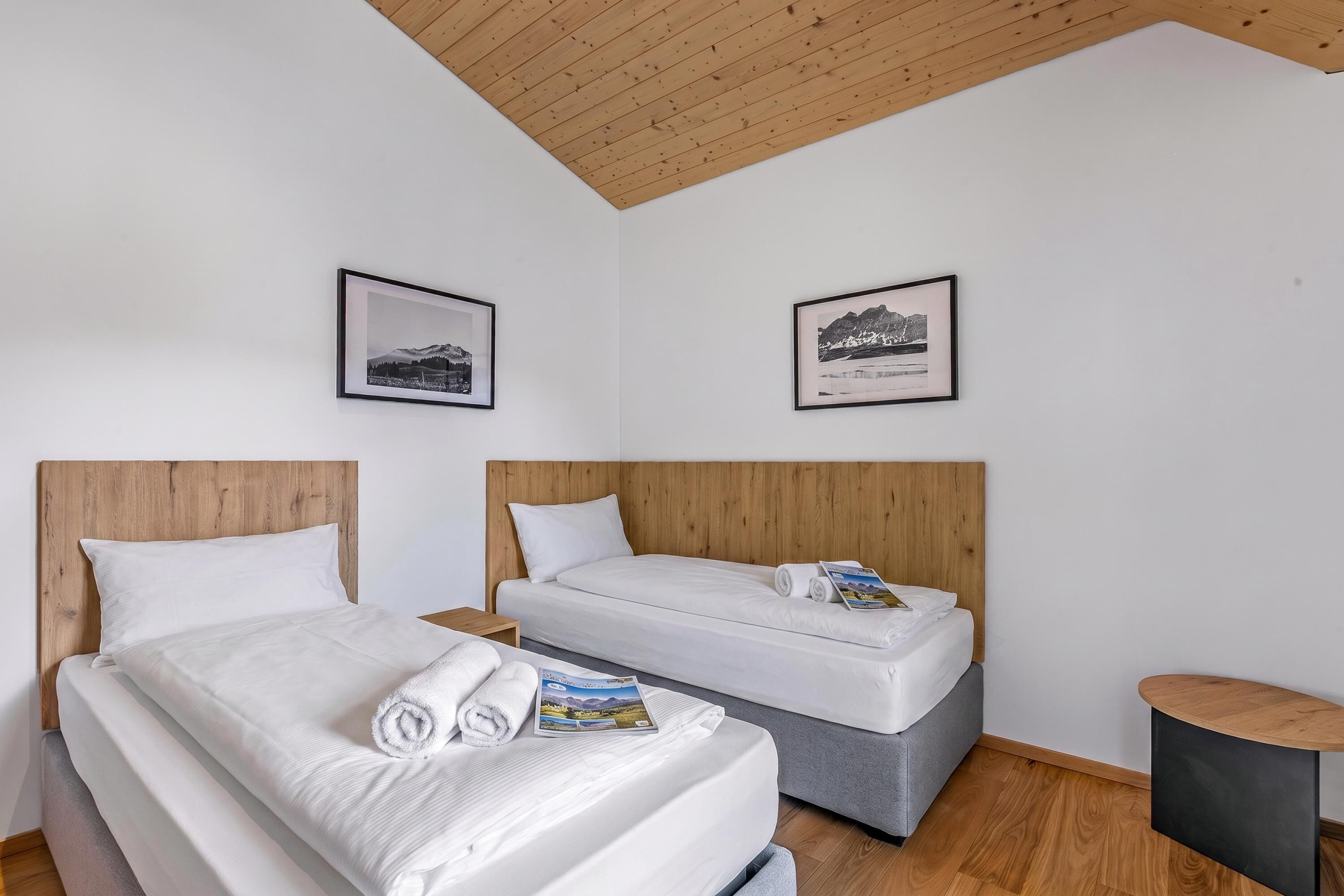 Habitación de hotel con dos camas, cabeceros de madera, ropa de cama blanca y dos cuadros en la pared.