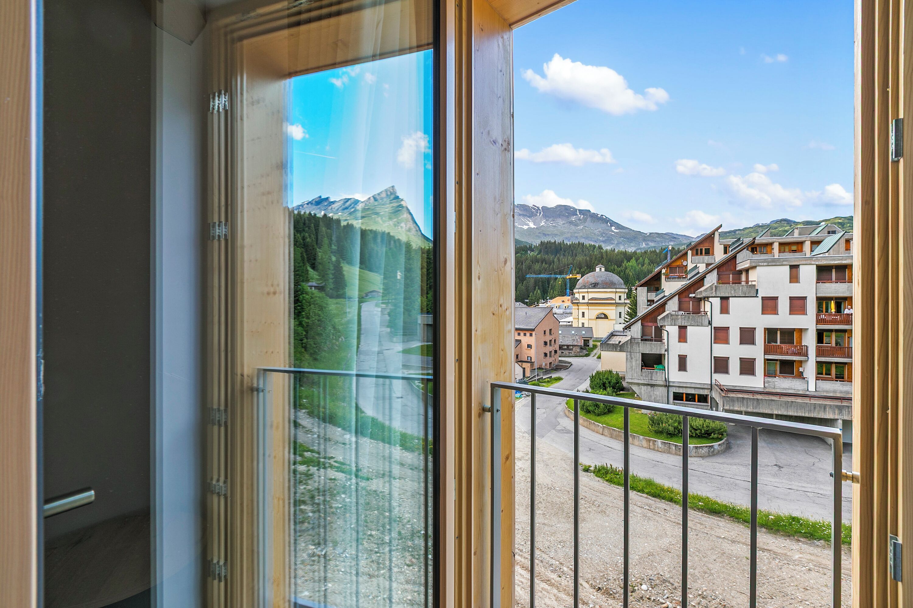 Vista desde un balcón con montañas al fondo, una zona pavimentada y edificios con balcones.