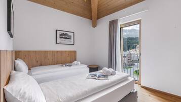 Habitación de hotel con dos camas, techo de madera, un cuadro en la pared y ventana con vistas a edificios y montañas.