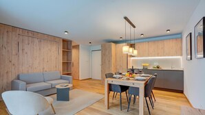 Ein modernes Wohnzimmer mit einer Couch, einem Esstisch für vier Personen und einer Küchenzeile mit Holzschränken und Pendelleuchten.