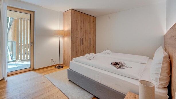 Ein Schlafzimmer mit einem Bett, einem Nachttisch, einer Stehlampe und einem Holzschrank.