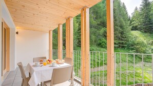 Ein überdachter Essbereich im Freien mit einem für das Frühstück gedeckten Tisch, mit Blick auf eine bewaldete Landschaft.