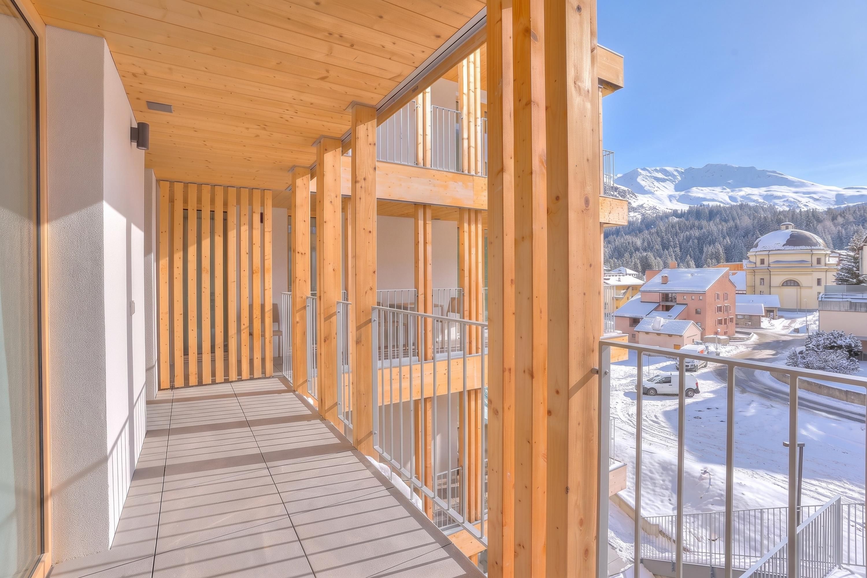 Ein Holzbalkon mit Blick auf einen verschneiten Berg und Gebäude.