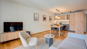Ein modernes Wohnzimmer mit Flachbildfernseher, einer Couch, einem Esstisch mit Stühlen und einer Küchenzeile mit Holzausbau.