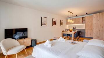 A modern hotel room with a large bed, a TV, a desk with a chair, and a dining area.