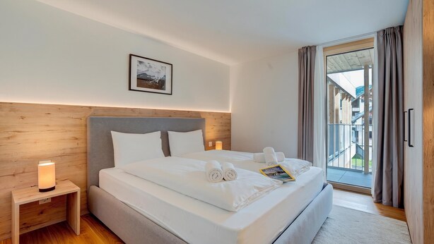 Ein Hotelzimmer mit einem großen Bett, einem Nachttisch mit Lampe, einem gerahmten Bild an der Wand und Blick durch eine Schiebetür nach draußen.