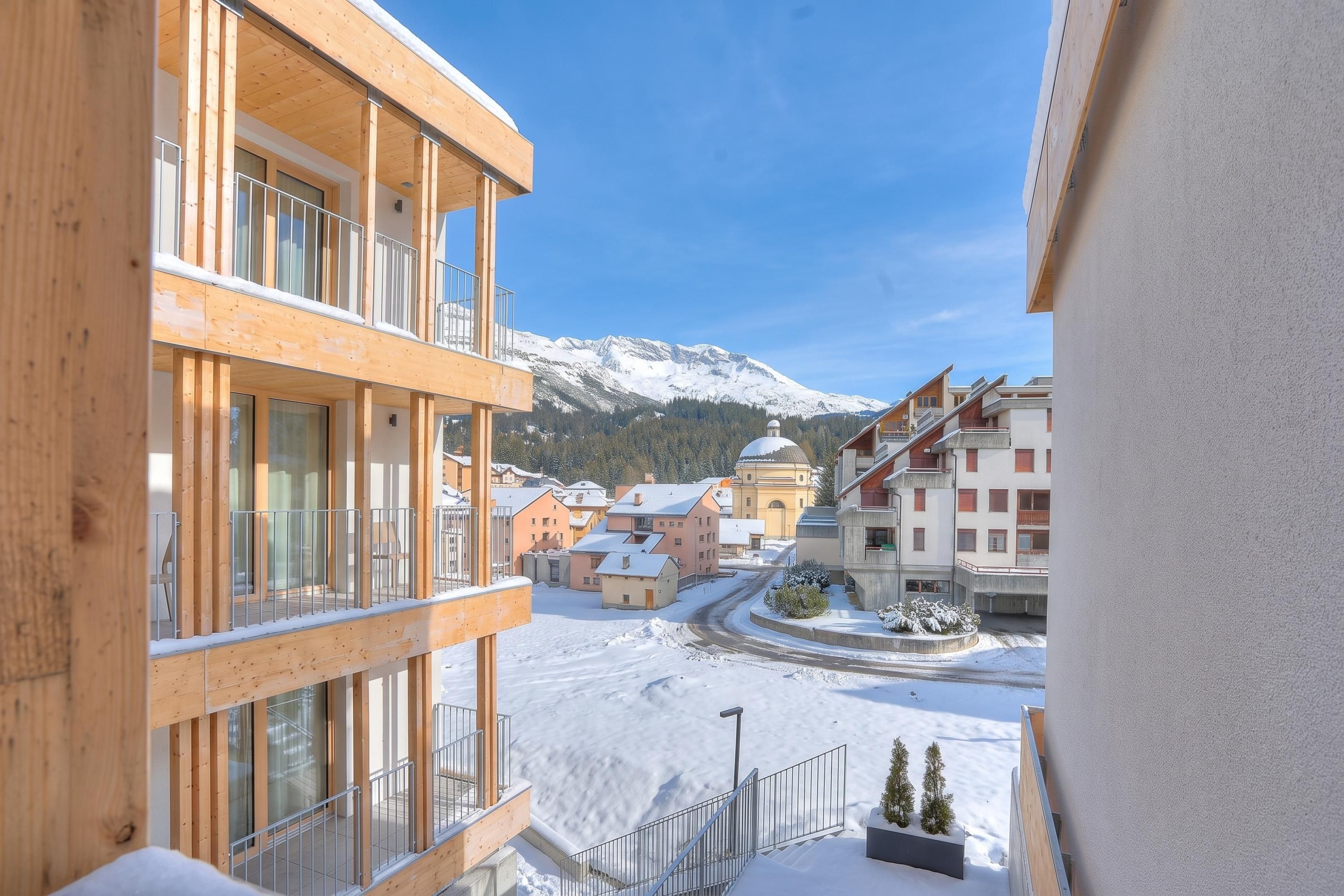 Un carrer cobert de neu amb edificis, incloent una construcció de fusta amb balcons i un edifici amb forma de cúpula al fons.