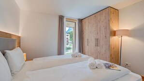 Ein Hotelzimmer mit zwei Betten, einem Holzschrank, einem Nachttisch mit Lampe und einem Fenster mit Vorhängen.