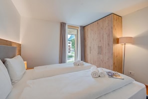 Une chambre d’hôtel avec deux lits, une armoire en bois, une table de chevet avec une lampe et une fenêtre avec des rideaux.