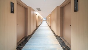 Un long couloir étroit d’hôtel, avec des murs en bois, des portes numérotées et un tapis à rayures bleues.