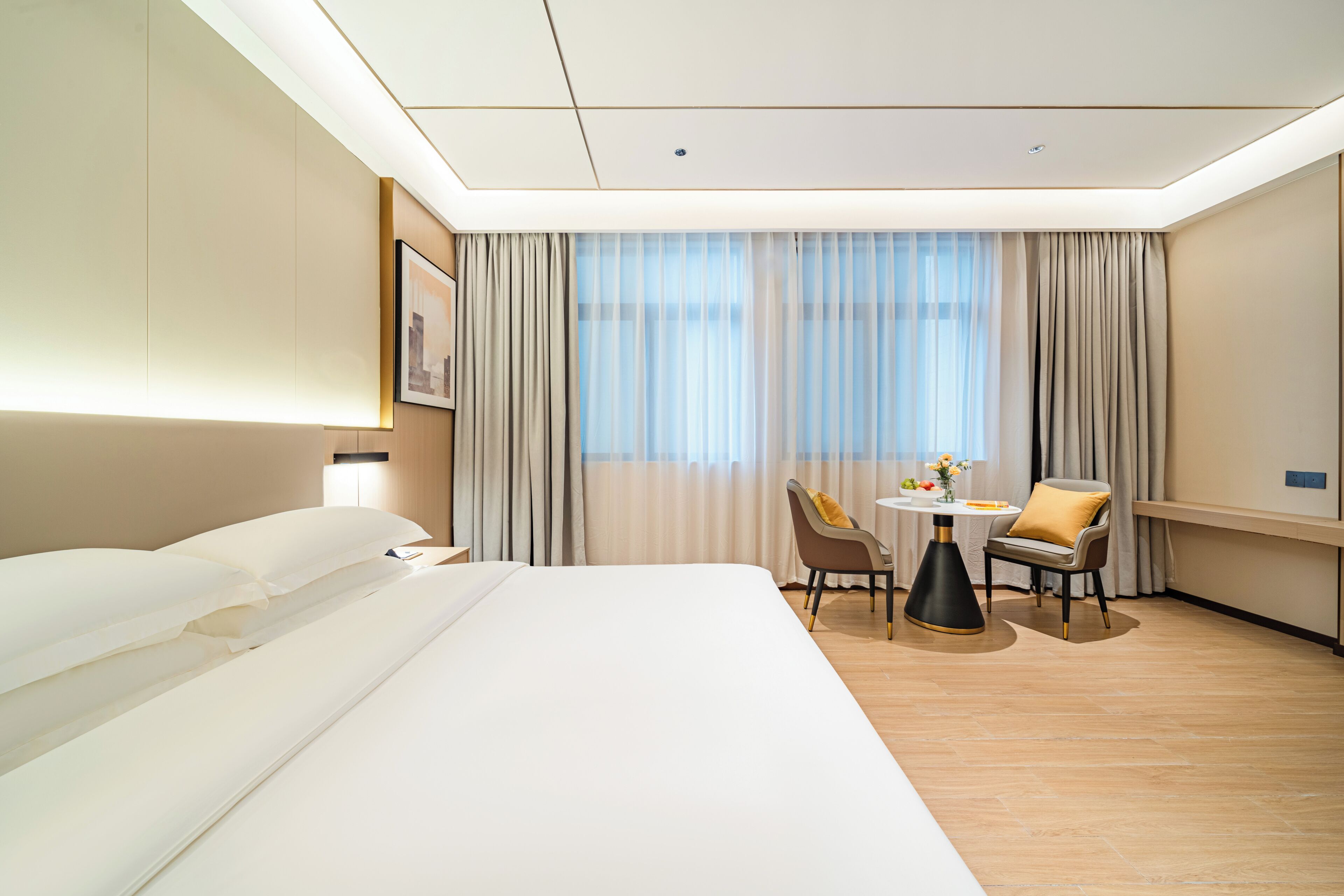 Habitación de hotel con una cama grande, un escritorio con dos sillas, una ventana con cortinas y un cuadro en la pared.
