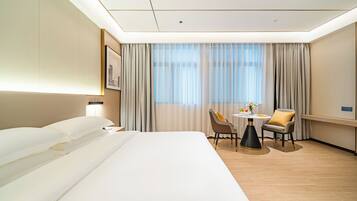 Habitación de hotel con una cama grande, un escritorio con dos sillas, una ventana con cortinas y un cuadro en la pared.