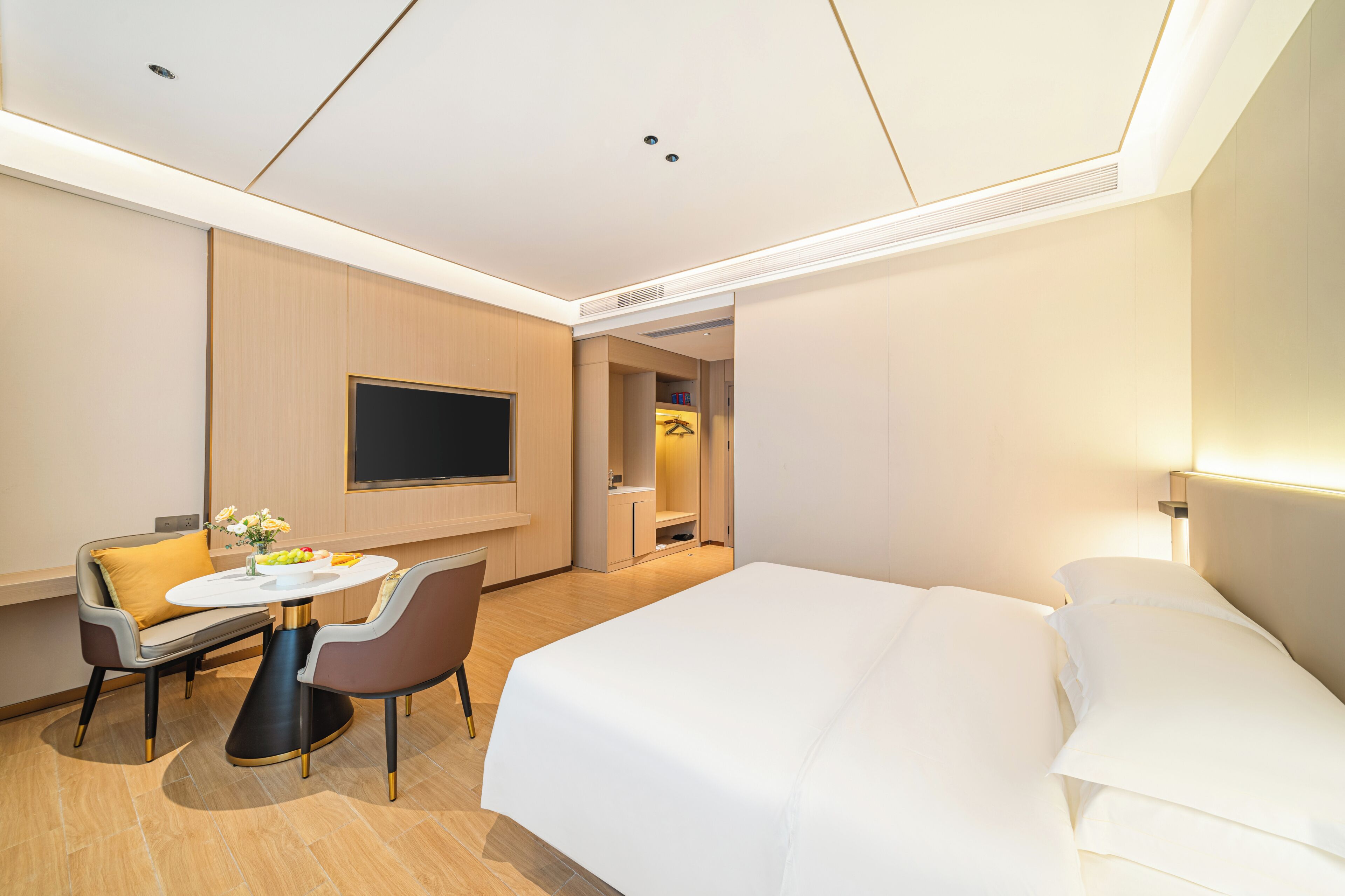 Quarto de hotel com uma cama, televisão, escrivaninha com cadeira e uma pequena mesa com uma tigela de frutas.