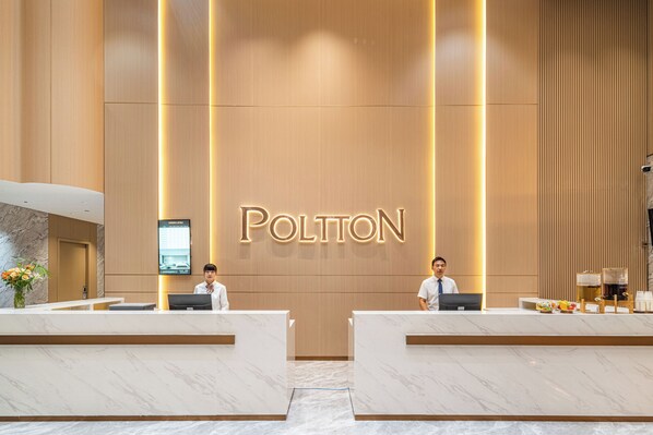 A hotel reception area with a modern design, featuring a large illuminated sign that reads 'POLTON' and two receptionists at their desks.