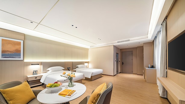 Une chambre d’hôtel moderne équipée d’un lit, de deux tables de chevet, d’un coin salon avec une table et d’un grand téléviseur à écran plat.