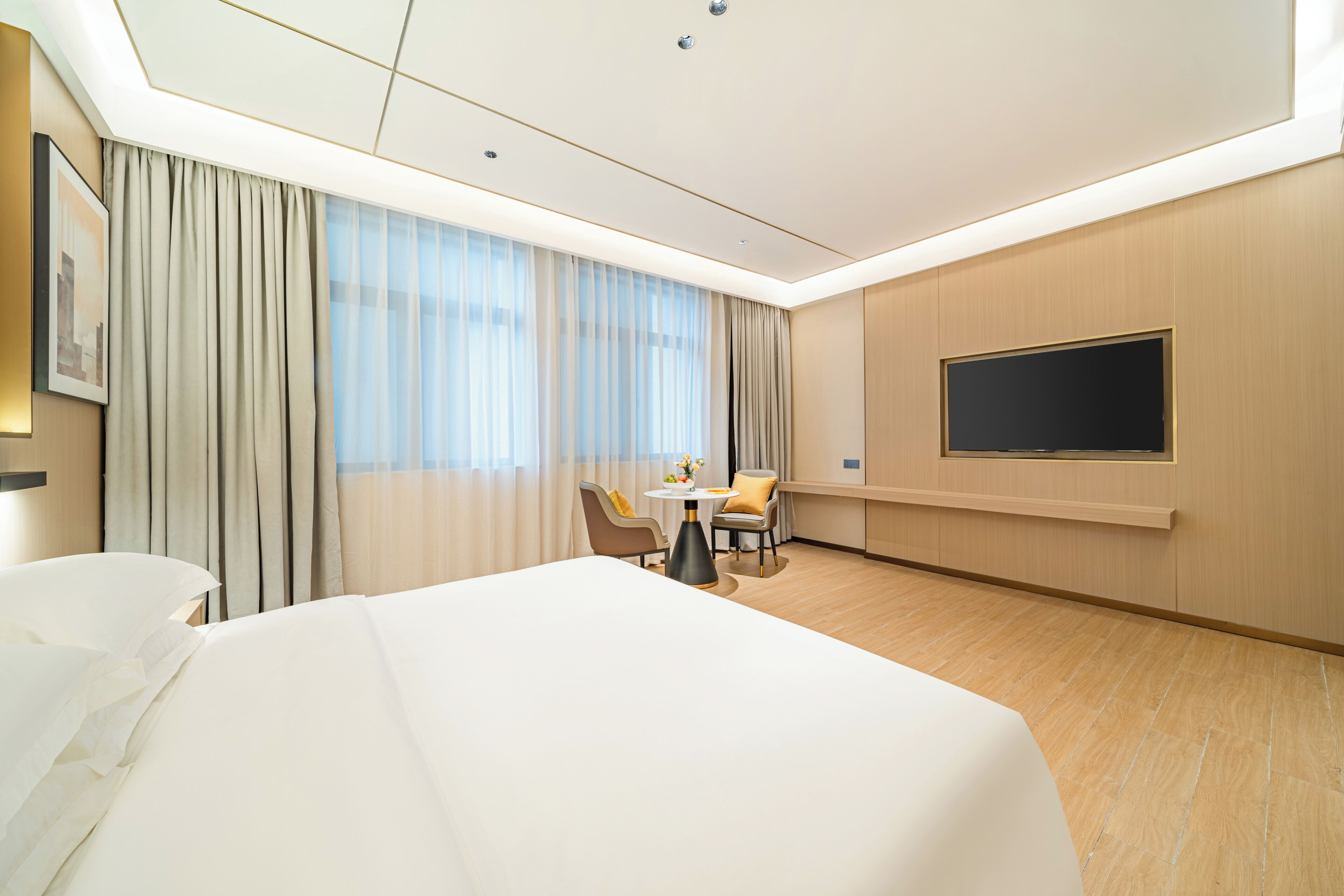 Habitació d'hotel amb llit, escriptori, cadira, televisió i finestra amb cortines.