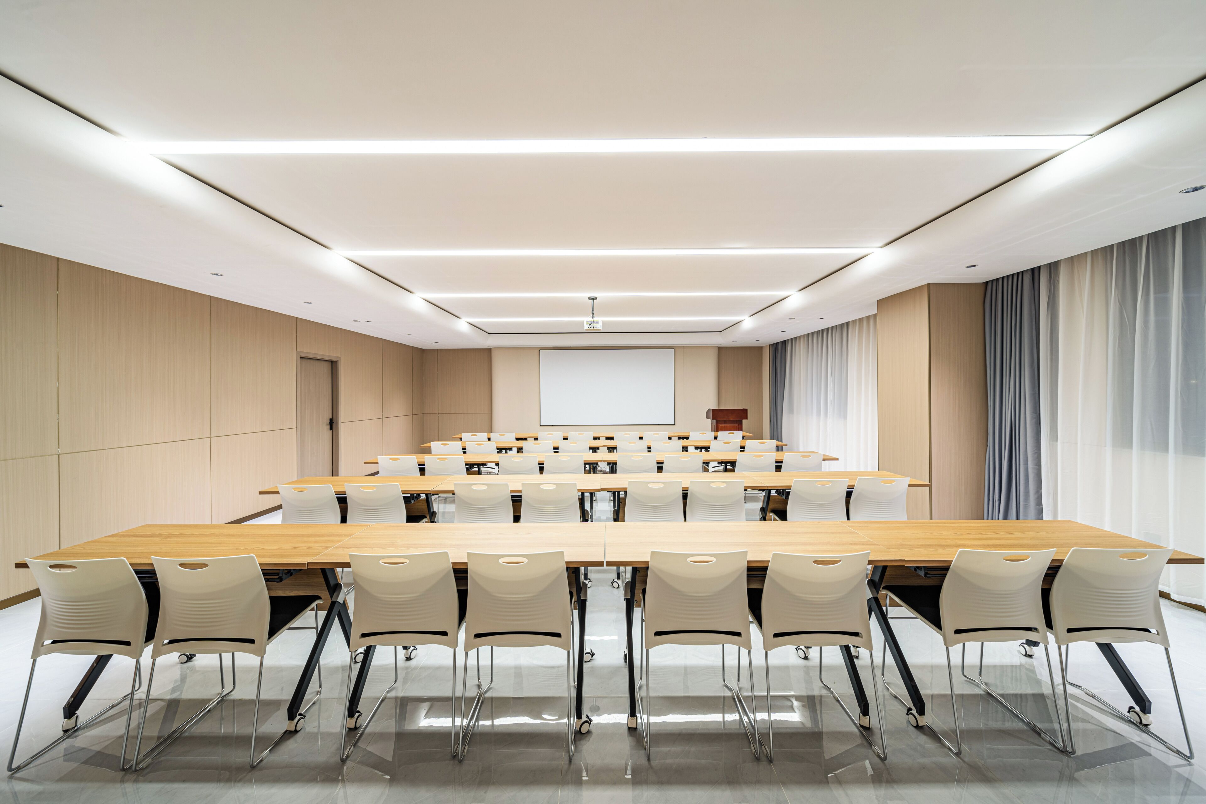 A conference room with a long table, chairs, a projector screen, and a podium.