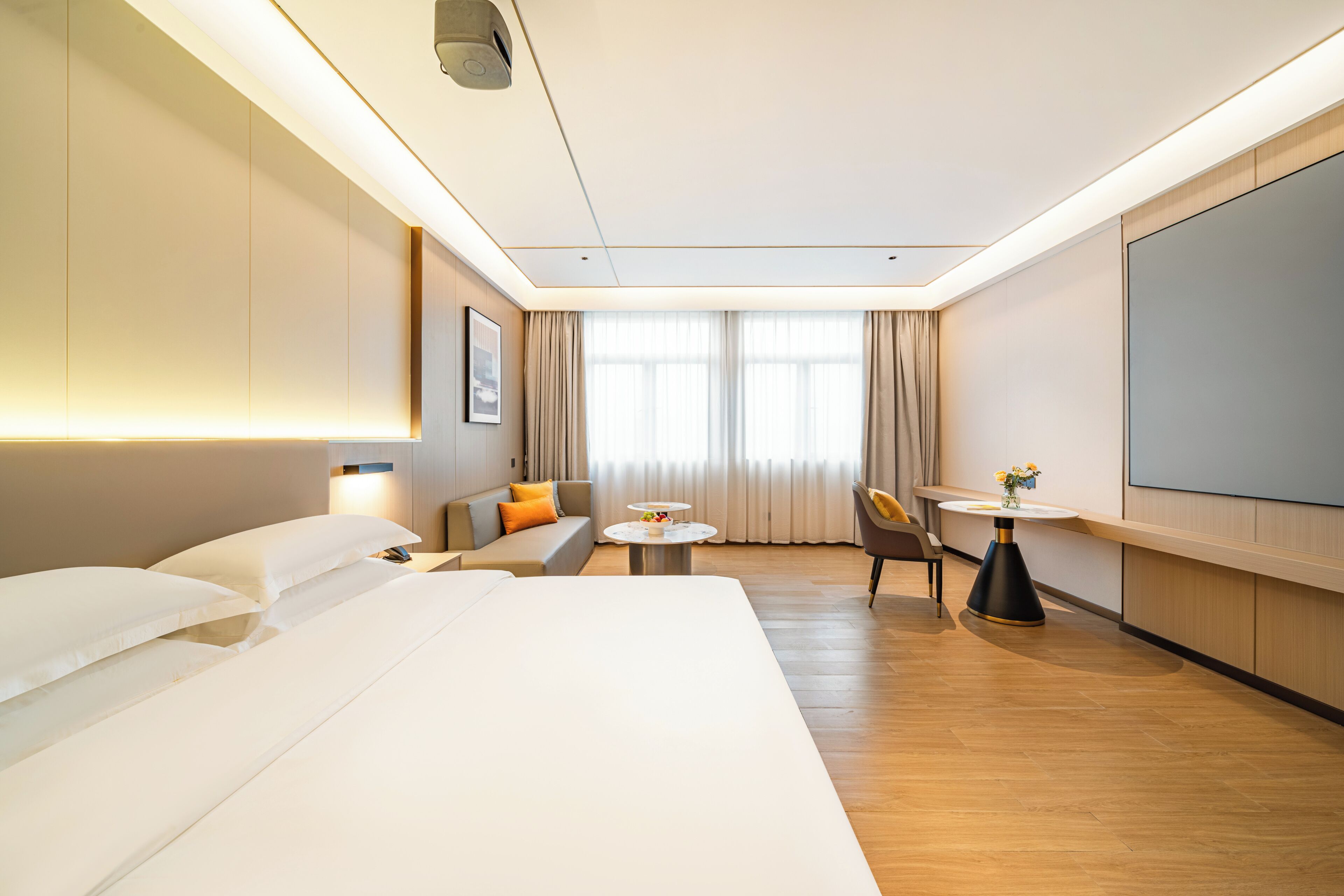A hotel room with a bed, a sofa, a dining table, and a TV.
