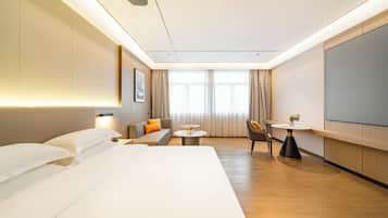 A hotel room with a bed, a sofa, a dining table, and a TV.