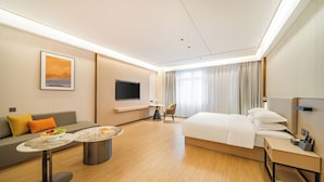 Une chambre d’hôtel moderne équipée d’un lit, d’un canapé, d’une télévision, d’une petite table avec des fruits et d’une chaise.