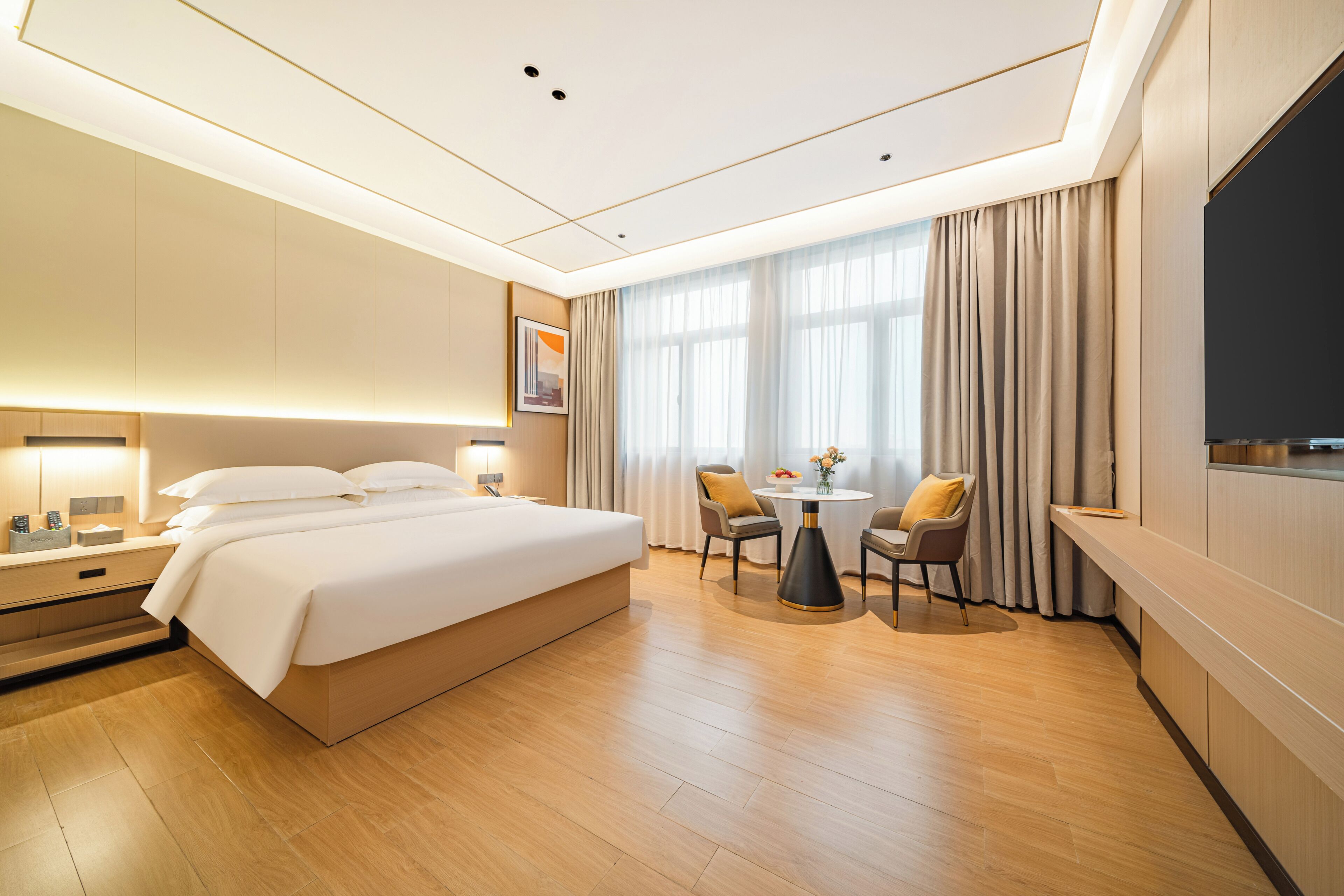 A hotel room with a large bed, a desk, a chair, a small table with a vase, and a TV.