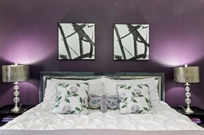 Un lit agrémenté d’oreillers à motifs floraux, d’une tête de lit et de deux tableaux abstraits accrochés au mur.
