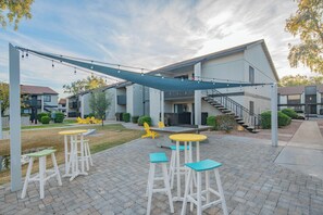 Un espace extérieur aménagé en patio, doté d’un coin salon couvert, d’un escalier menant à un niveau supérieur et offrant une vue sur les bâtiments adjacents.