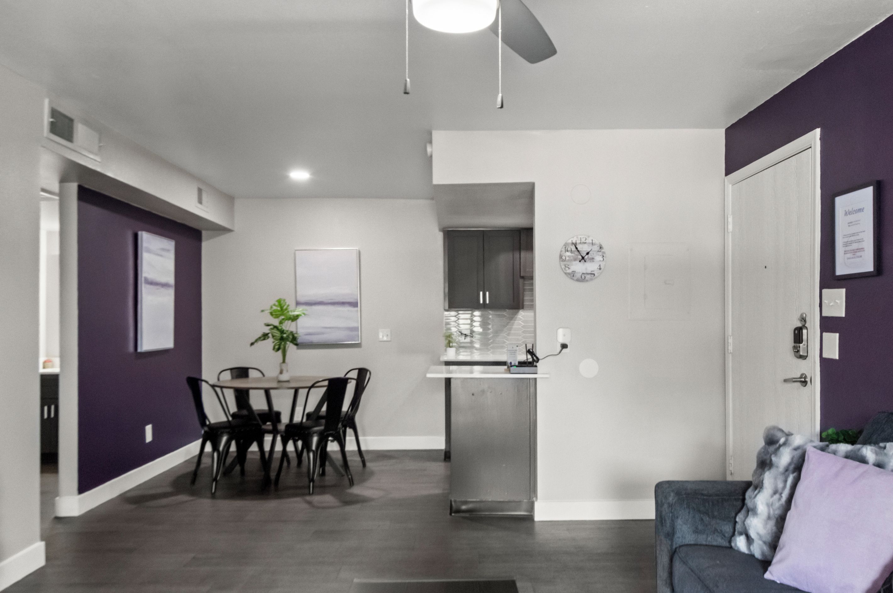 Een moderne woonkamer met een eethoek, een keuken op de achtergrond, en een deur naar een andere kamer.