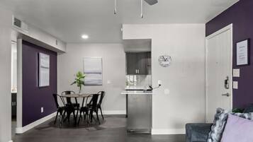 Een moderne woonkamer met een eethoek, een keuken op de achtergrond, en een deur naar een andere kamer.