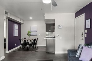 Un salon moderne avec un coin repas, une cuisine à l’arrière-plan et une porte donnant sur une autre pièce.